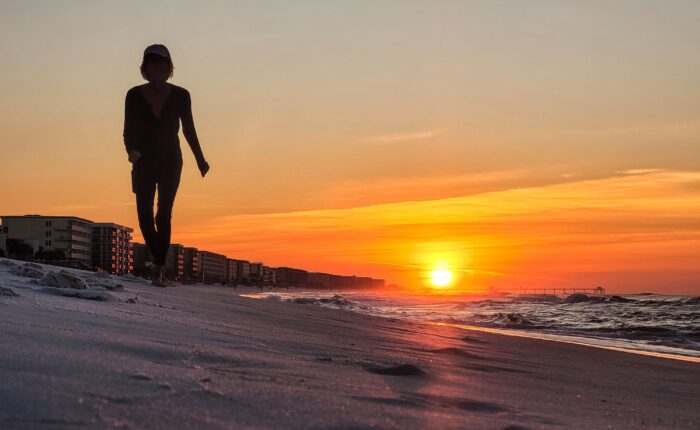 silhouetted woman walking down a sandy beach