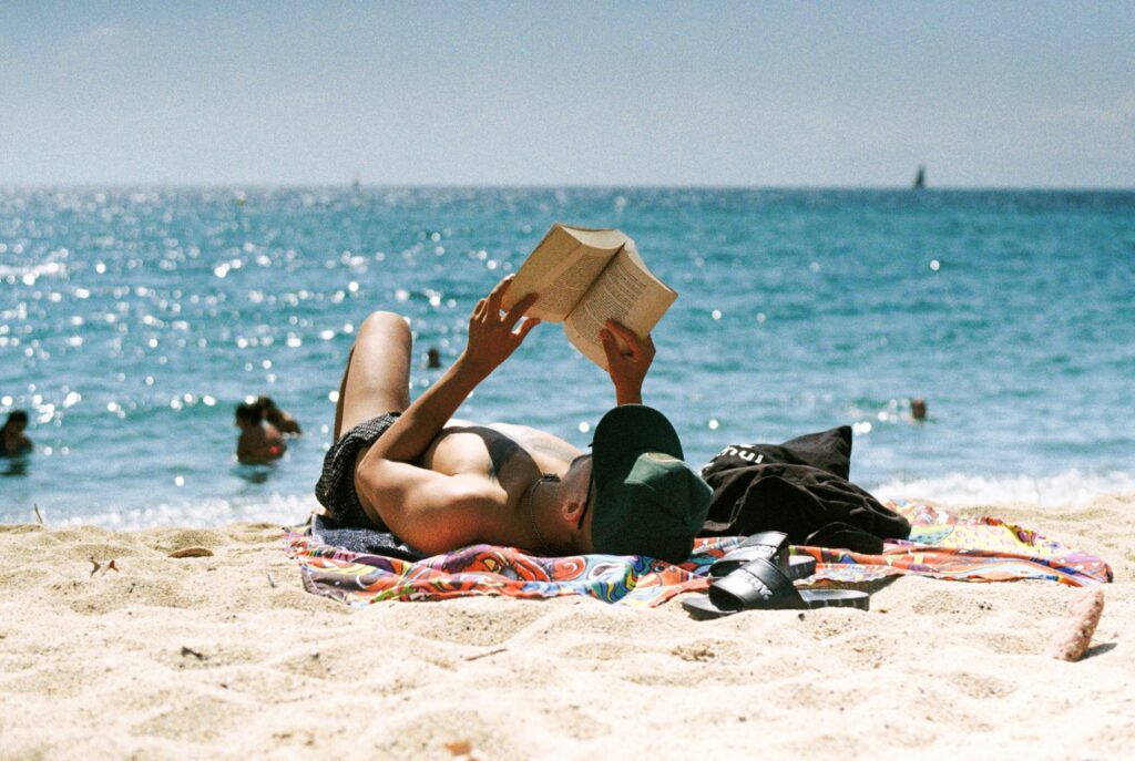 a person laying on the sand at the beach reading a book