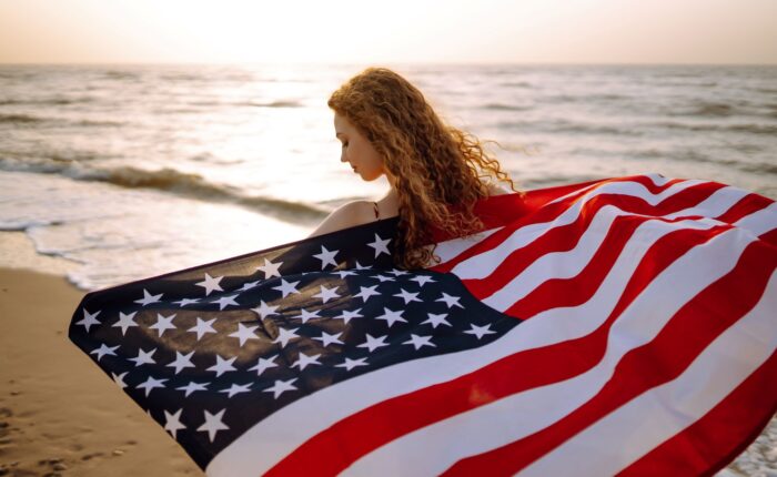 Young woman with american flag on the beach at sunset.